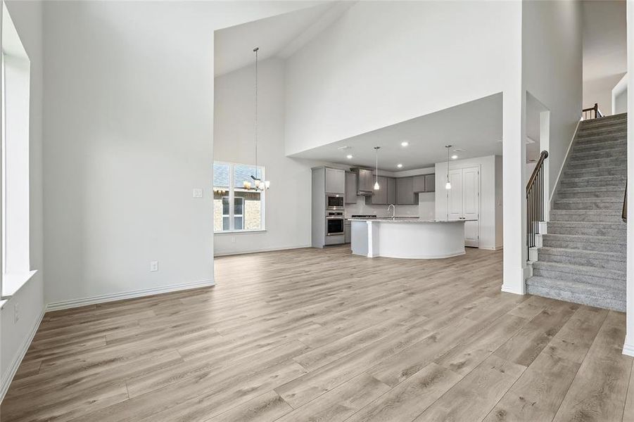Unfurnished living room with light wood-style floors, stairway, high vaulted ceiling, and a chandelier Unfurnished living room with light wood-style floors, stairway, high vaulted ceiling, and a chandelier