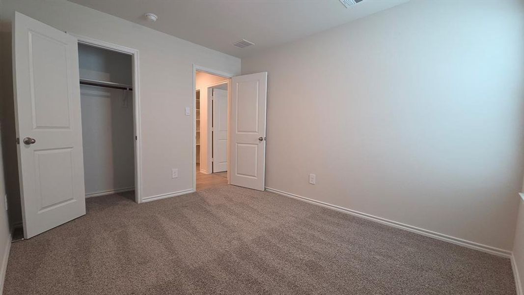 Carpeted interior room featuring neutral wall paint, white trim, and a double-door closet with a hanging rod