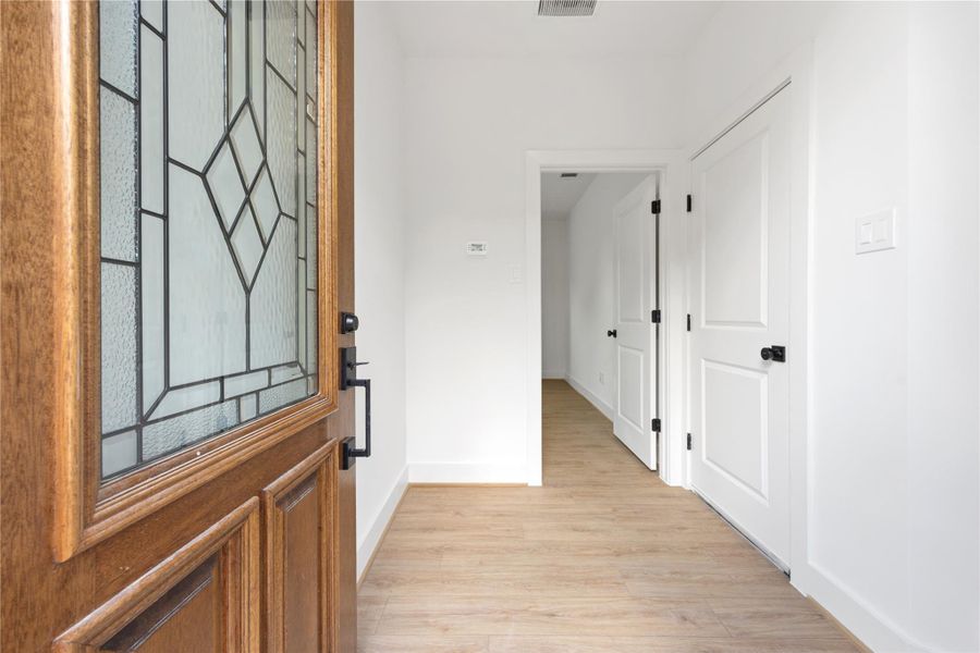 A welcoming entry sets the tone with a warm wood front door featuring decorative glass, crisp white walls, black hardware, and light wood-look flooring. The bright foyer offers a clean modern first impression, with nearby storage and easy access into the home’s flexible first-floor layout.