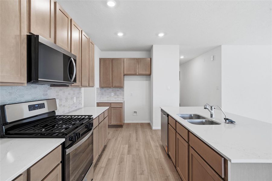 This bright, open kitchen is a chef's delight, complete with a large island, quartz countertops, Woodmont Dakota cabinets in Barley stain, Whirlpool stainless steel appliances, and modern Daltile backsplash.