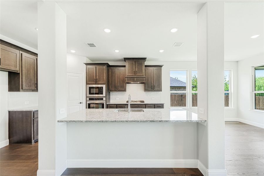 Kitchen with granite island, dark wood cabinets, stainless steel appliances, and hardwood floors Kitchen with granite island, dark wood cabinets, stainless steel appliances, and hardwood floors