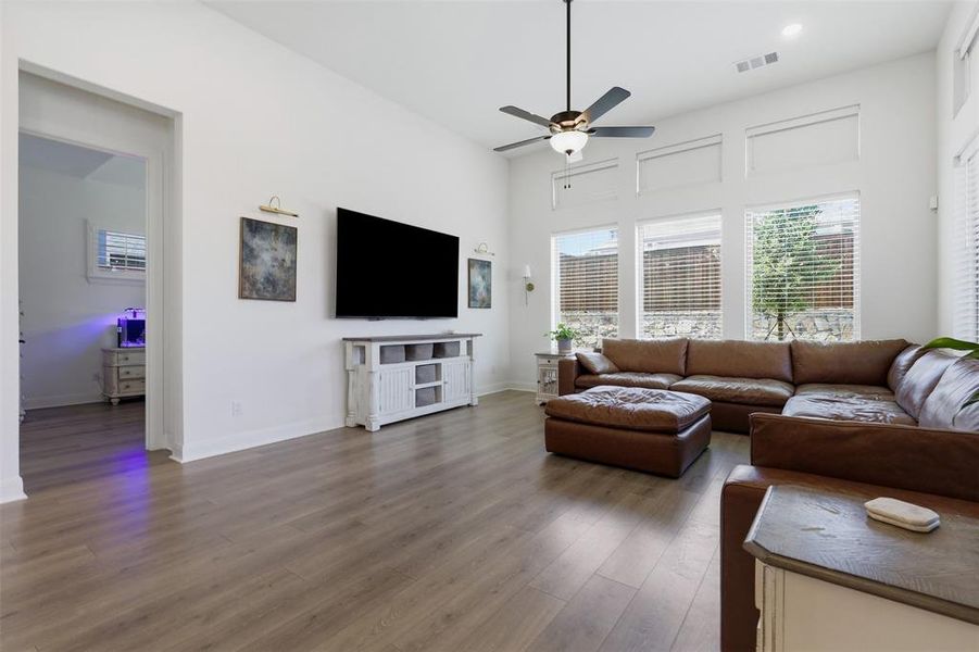 Bright living area with high ceilings, recessed lighting, wood-finish flooring, and multiple windows with blinds Bright living area with high ceilings, recessed lighting, wood-finish flooring, and multiple windows with blinds