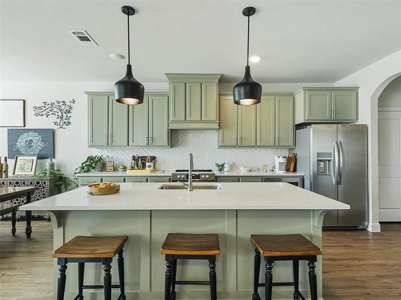 Kitchen featuring stainless steel refrigerator with ice dispenser, a center island with sink, tasteful backsplash, and hanging light fixtures