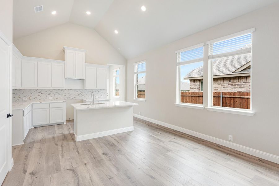 Open kitchen with white cabinets, center island, vaulted ceiling, and light wood floors
