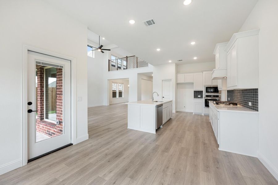 Open-concept kitchen with white cabinets, center island, and light wood floors with two-story ceiling Open-concept kitchen with white cabinets, center island, and light wood floors with two-story ceiling