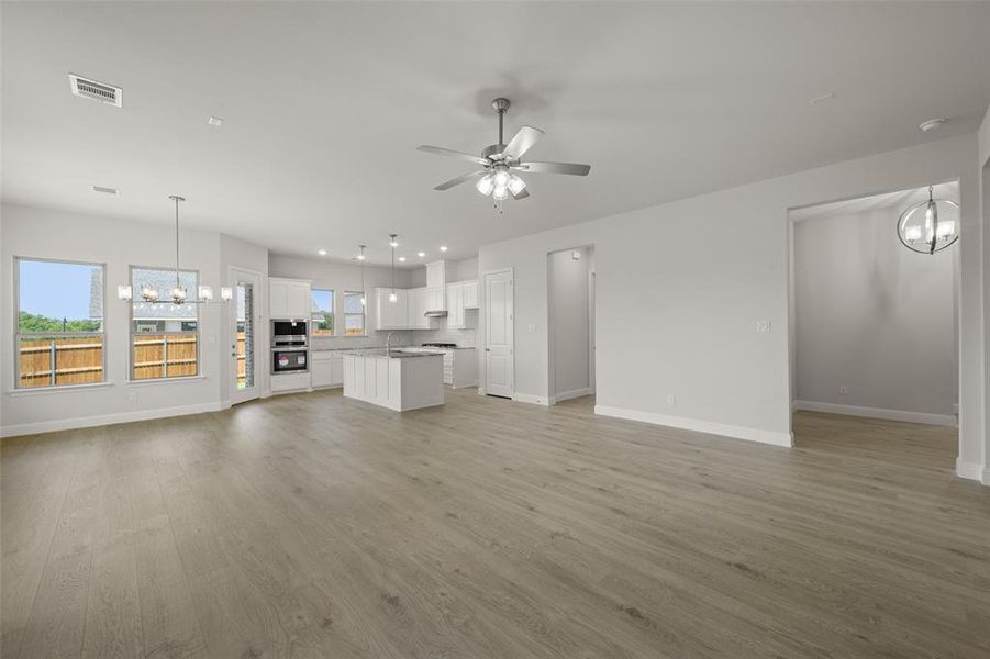 Unfurnished living room with a chandelier, a ceiling fan, and light wood-style flooring Unfurnished living room with a chandelier, a ceiling fan, and light wood-style flooring