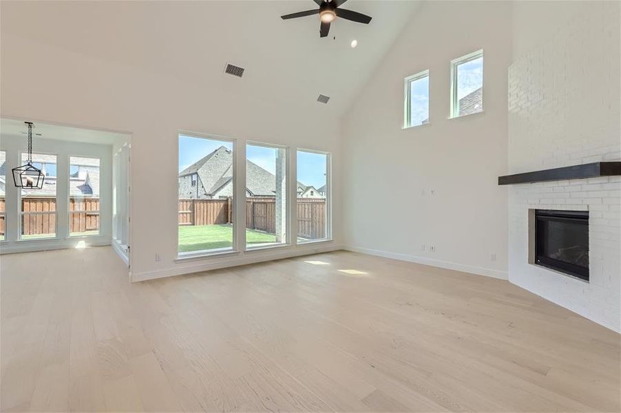 Unfurnished living room with high vaulted ceiling, ceiling fan, a fireplace, and light wood-type flooring