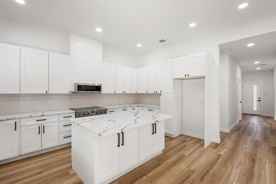 Kitchen with tasteful backsplash, white cabinetry, recessed lighting, light stone counters, and light wood-style floors Kitchen with tasteful backsplash, white cabinetry, recessed lighting, light stone counters, and light wood-style floors