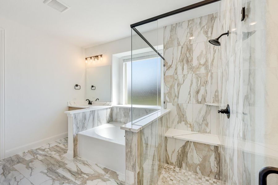 Master bathroom with marble tile walls, soaking tub, glass walk-in shower, and double vanity with black fixtures Master bathroom with marble tile walls, soaking tub, glass walk-in shower, and double vanity with black fixtures