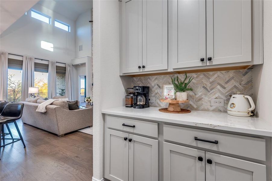 Bar with a high ceiling, light stone countertops, dark wood-style floors, tasteful backsplash, and white cabinets