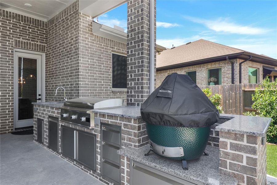 Beautiful outdoor kitchen featuring a built-in grill, sink, ample counter space, and dedicated space for a Big Green Egg, creating the perfect setup for outdoor cooking and entertaining