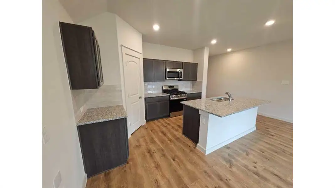 Modern kitchen featuring wood-finish flooring, dark wood-finish cabinetry, granite countertops, a stainless steel microwave and range, and recessed lighting