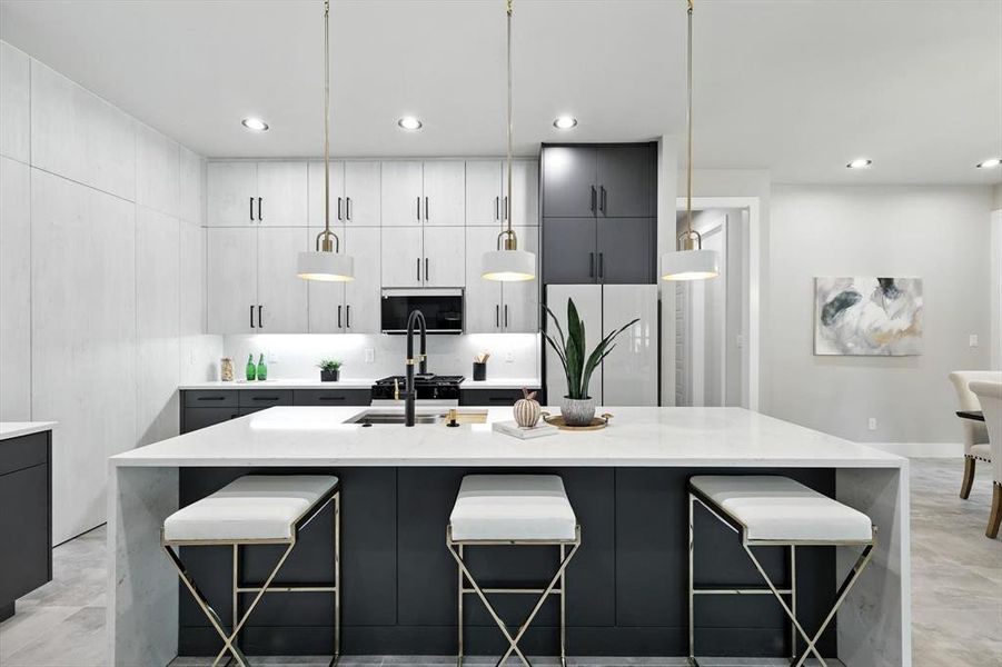 Kitchen with light stone counters, a breakfast bar, gray cabinets, a large island with sink, and pendant lighting