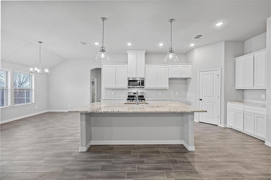Before it was furnished Kitchen featuring arched walkways, white cabinets, light stone countertops, hanging light fixtures, and recessed lighting Before it was furnished Kitchen featuring arched walkways, white cabinets, light stone countertops, hanging light fixtures, and recessed lighting