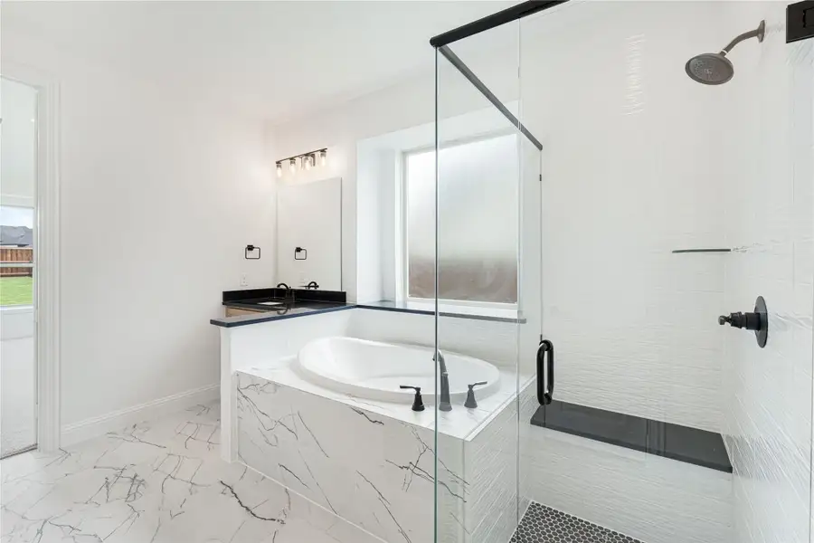 Master bathroom with marble soaking tub, glass walk-in shower, and black vanity countertop on white tile floors