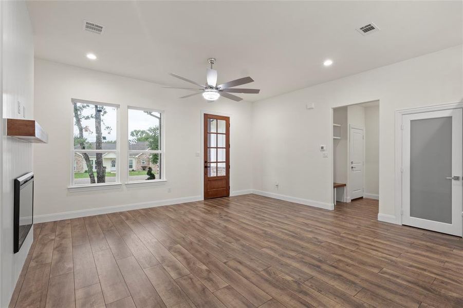 Spacious living area featuring wood-finish flooring, a modern ceiling fan, recessed lighting, and a contemporary fireplace with a wood mantle Spacious living area featuring wood-finish flooring, a modern ceiling fan, recessed lighting, and a contemporary fireplace with a wood mantle