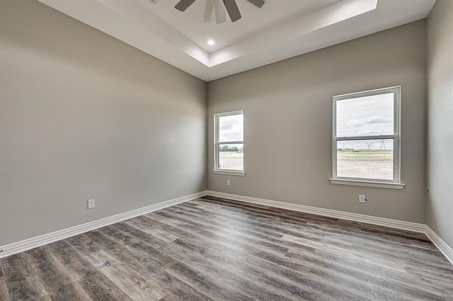 Unfurnished room with ceiling fan, wood-type flooring, and a tray ceiling