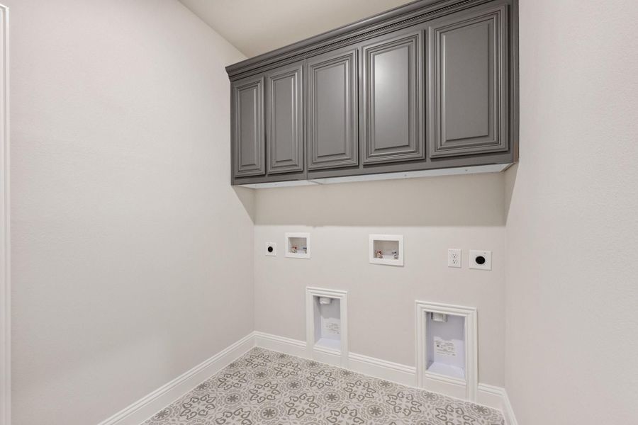 Laundry room with gray upper cabinets, washer and dryer hookups, and patterned tile floor Laundry room with gray upper cabinets, washer and dryer hookups, and patterned tile floor