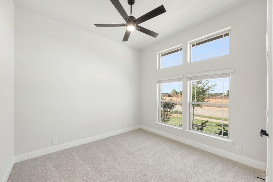 Empty bedroom with carpet flooring, black ceiling fan, and double windows overlooking a backyard