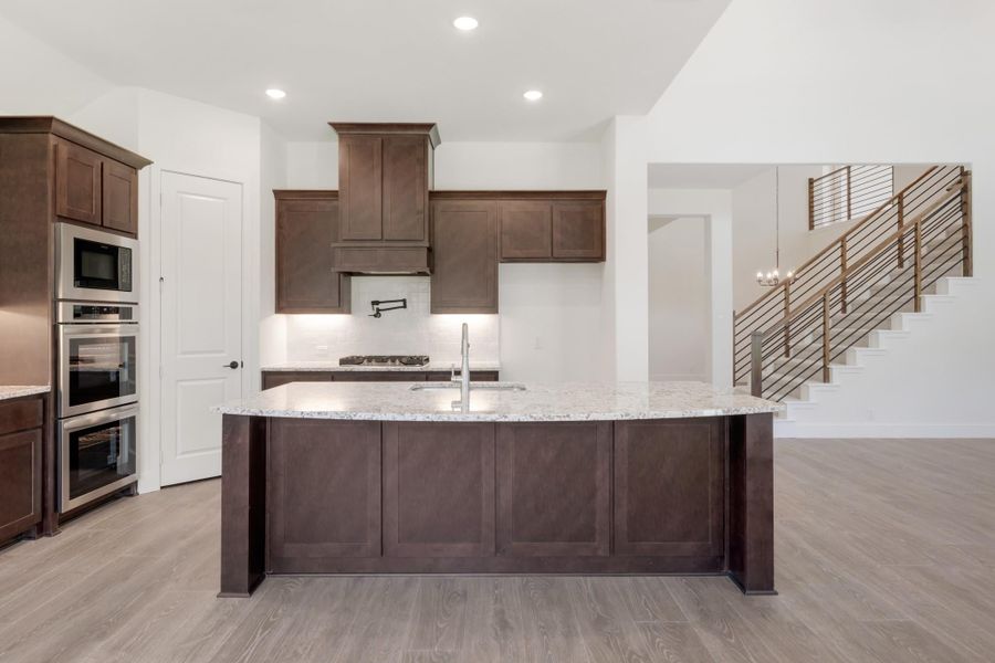 Kitchen with large island, granite countertops, dark wood cabinets, and stainless steel appliances on light hardwood floors