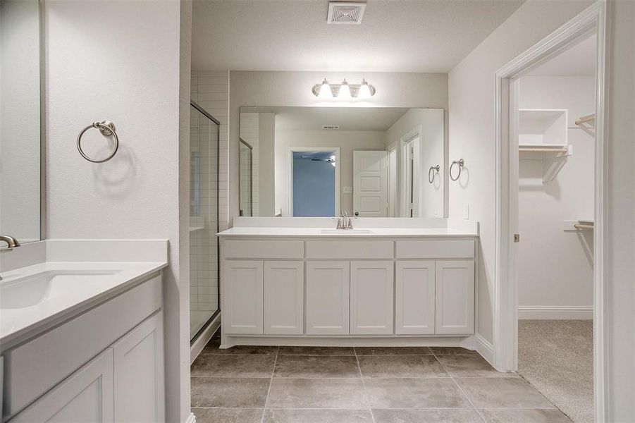 Full bath featuring a stall shower, two vanities, a sink, and visible vents