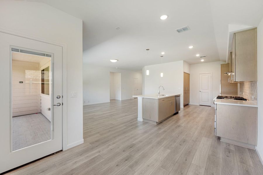 Open-concept kitchen with center island, light wood floors, and tan cabinets opening to living area Open-concept kitchen with center island, light wood floors, and tan cabinets opening to living area