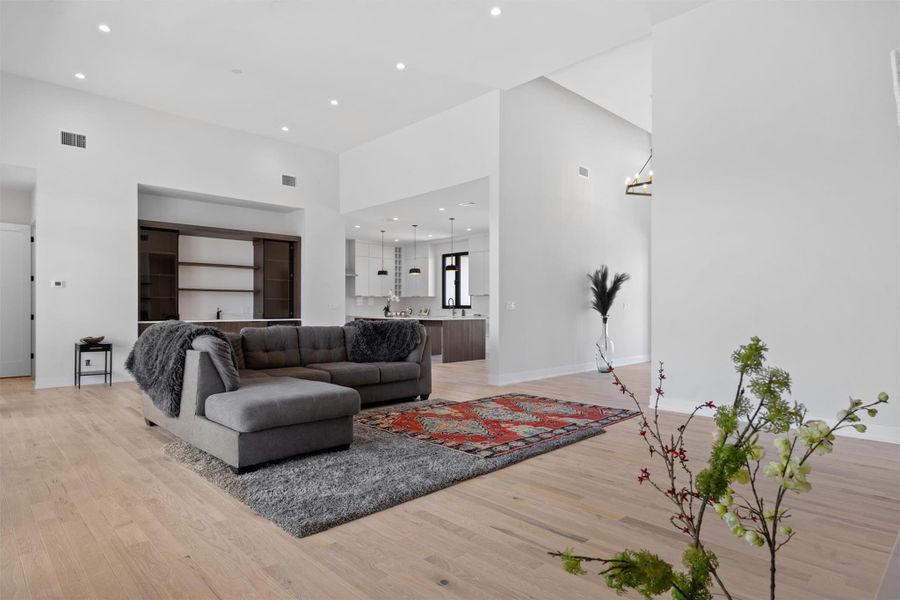 Living room featuring visible vents, recessed lighting, a high ceiling, light wood-style floors, and a chandelier