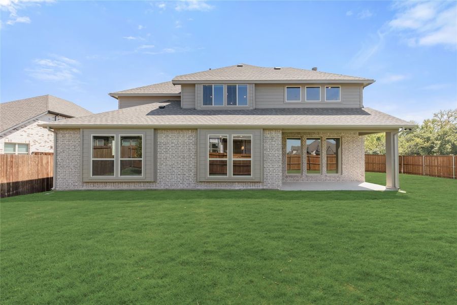 Two-story home rear view with brick exterior, covered patio, and large fenced backyard with green lawn. Two-story home rear view with brick exterior, covered patio, and large fenced backyard with green lawn.
