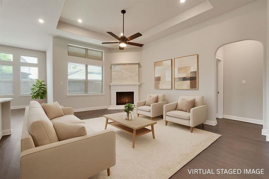 Living room with a raised ceiling, arched walkways, a fireplace with raised hearth, recessed lighting, and dark wood finished floors Living room with a raised ceiling, arched walkways, a fireplace with raised hearth, recessed lighting, and dark wood finished floors
