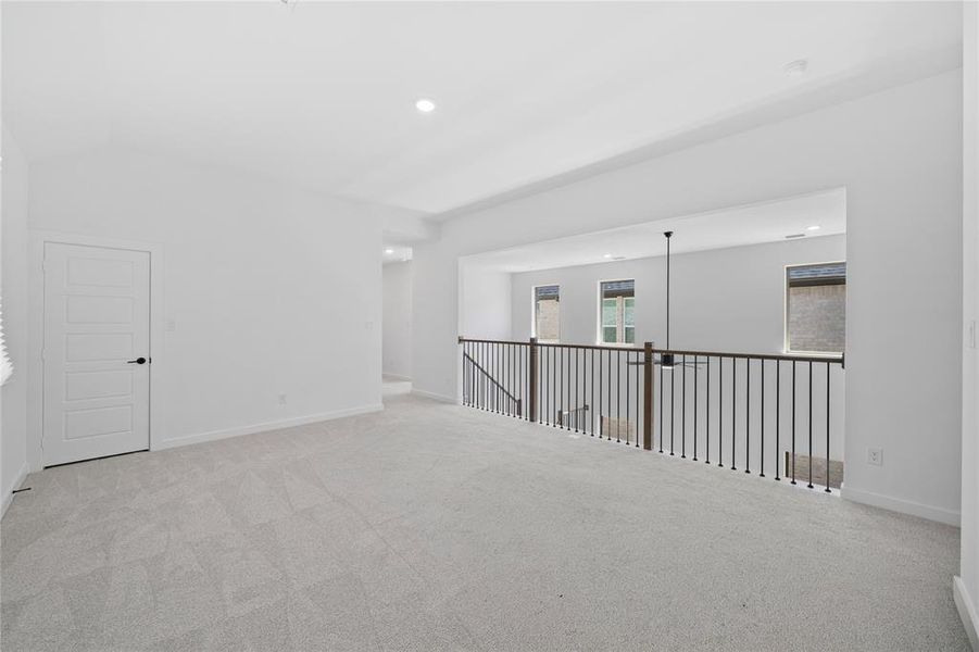 Spacious carpeted loft area featuring a modern black metal railing, contemporary pendant lighting, recessed ceiling lights, and a five-panel interior door with matte black hardware