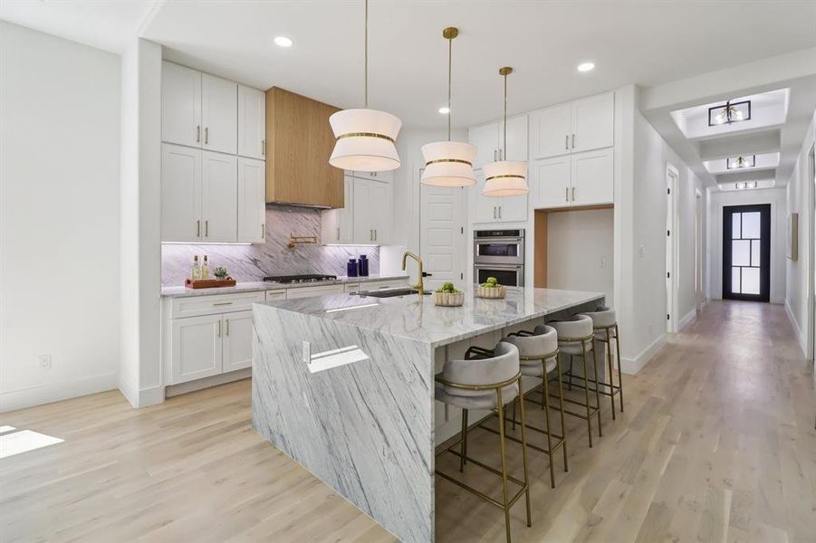 Kitchen with a large island, light wood finished floors, white cabinets, light stone countertops, and recessed lighting