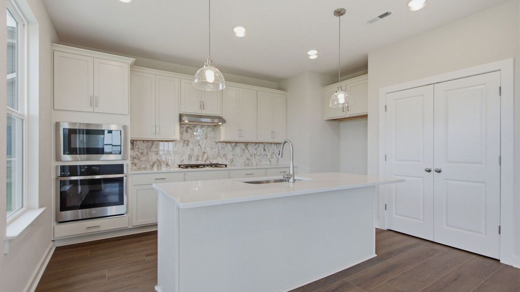 Kitchen with pantry, island, white cabinets, tile backsplash, and gas cooktop