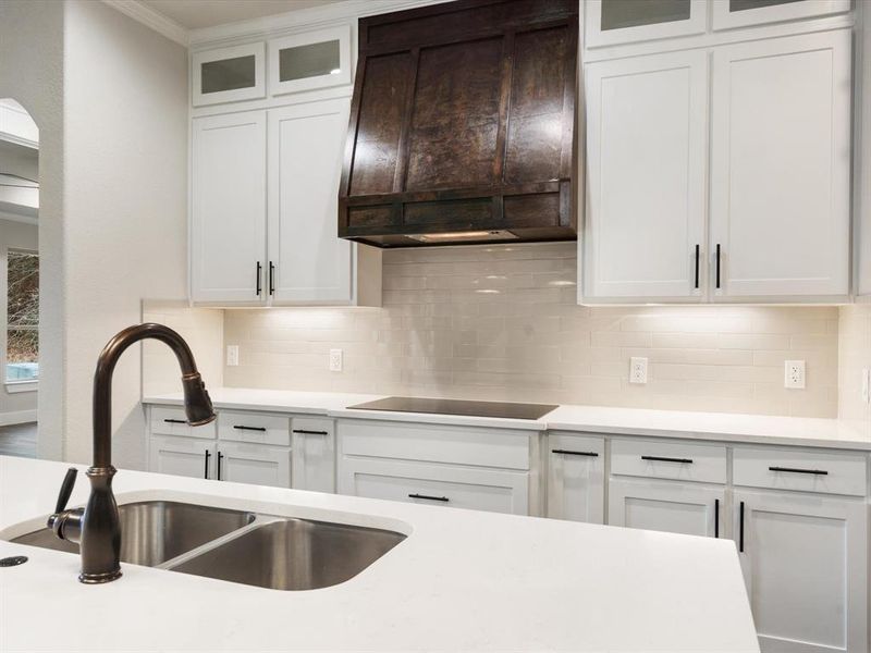 Kitchen with black stovetop, tasteful backsplash, sink, and white cabinets