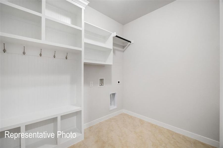 This utility room features built-in white shelving with storage cubbies and coat hooks, a clothes hanging rod, and light-toned floor tiles