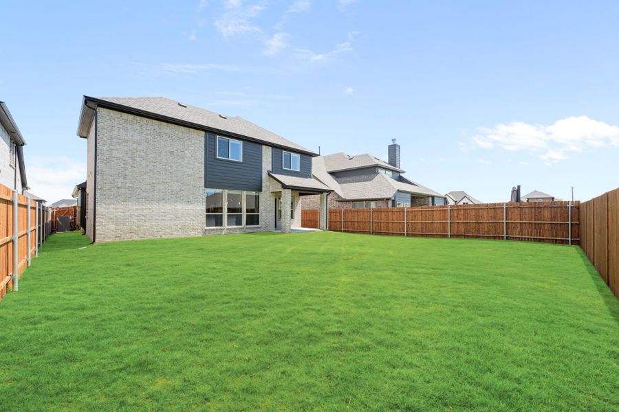 Backyard of two-story brick home with large green lawn and wood privacy fence