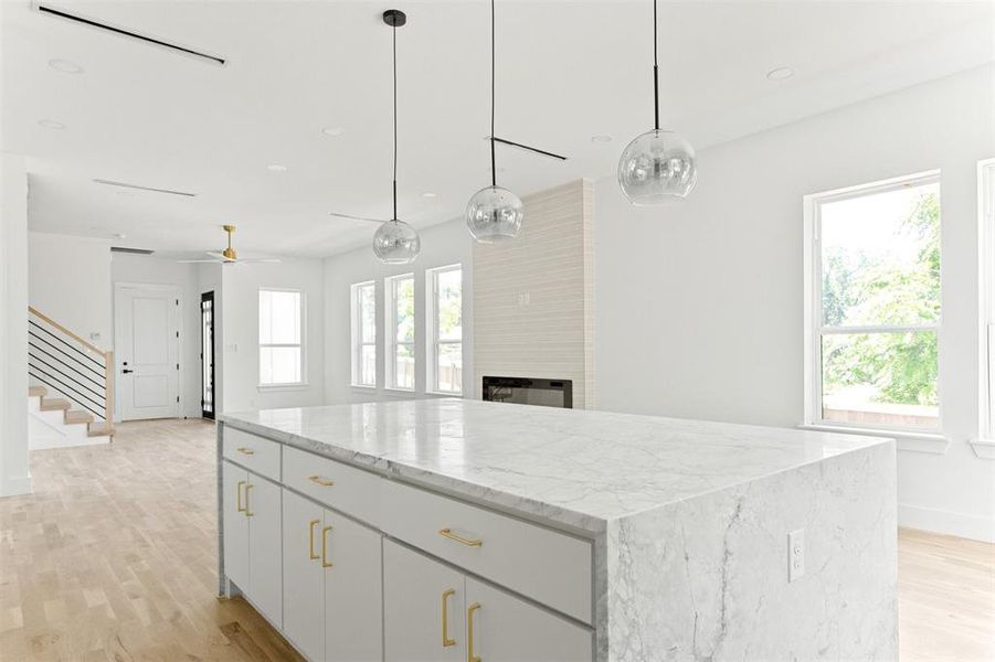 Kitchen with ceiling fan, a fireplace, light wood-type flooring, pendant lighting, and a kitchen island