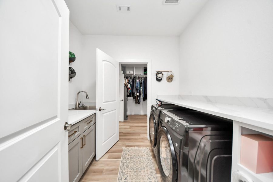 Spacious laundry room featuring ample countertop space, cabinets for storage and organization, a dedicated sink and convenient access to an adjacent walk-in closet. Spacious laundry room featuring ample countertop space, cabinets for storage and organization, a dedicated sink and convenient access to an adjacent walk-in closet.