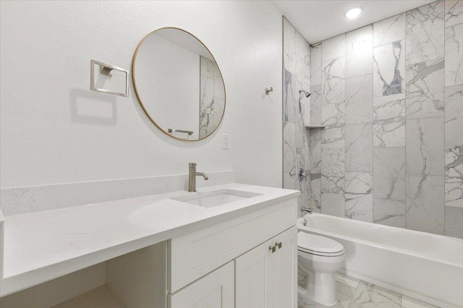 A refined bathroom featuring a contemporary vanity, large circular mirror, and marble-inspired tile surrounding the tub. A refined bathroom featuring a contemporary vanity, large circular mirror, and marble-inspired tile surrounding the tub.