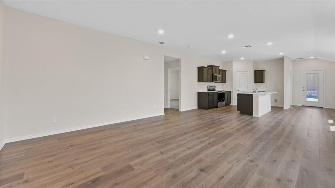 Open-concept living space featuring wood-finish flooring, recessed lighting, and vaulted ceilings