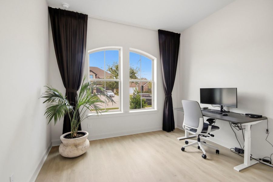 Welcoming home office/bedroom with large arched windows, sleek flooring, and a modern desk setup, perfect for productivity and comfort.