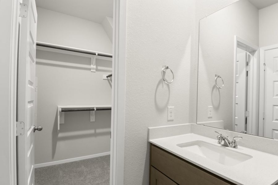 Image of a primary bathroom with a connecting walk in closet and a white vanity
