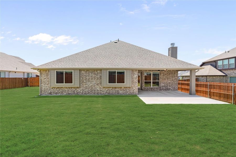 Rear view of single-story brick home with covered patio, large green lawn, and wood privacy fence.