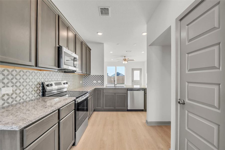 Kitchen with stainless steel appliances, light wood-type flooring, light stone counters, recessed lighting, and a ceiling fan