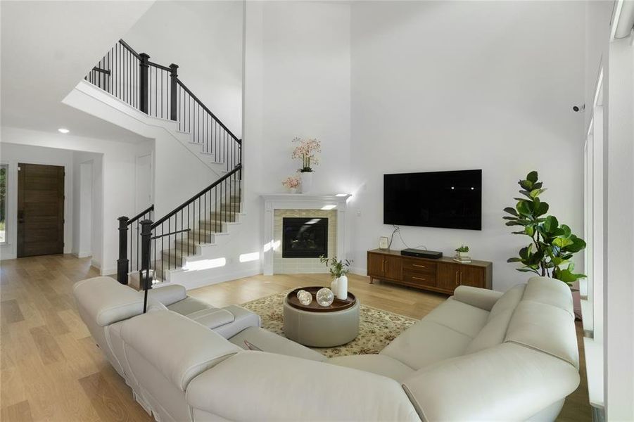 Two-story living area featuring wood-finish flooring, a contemporary fireplace with a stone surround and white mantel, and a multi-level staircase with dark wood newel posts and black iron balusters