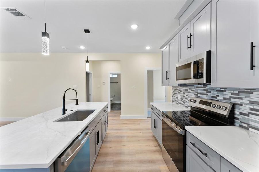 Kitchen featuring sink, appliances with stainless steel finishes, hanging light fixtures, tasteful backsplash, and an island with sink