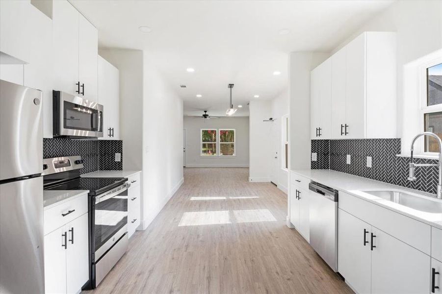 Kitchen featuring ceiling fan, backsplash, white cabinetry, and appliances with stainless steel finishes