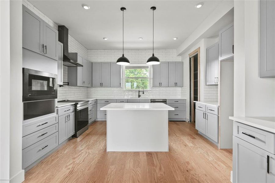 Kitchen with stainless steel electric range, black microwave, wall chimney exhaust hood, decorative backsplash, and gray cabinetry Kitchen with stainless steel electric range, black microwave, wall chimney exhaust hood, decorative backsplash, and gray cabinetry