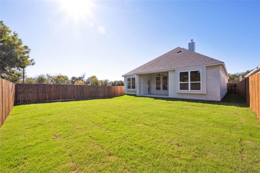 Back of house featuring ceiling fan and a yard