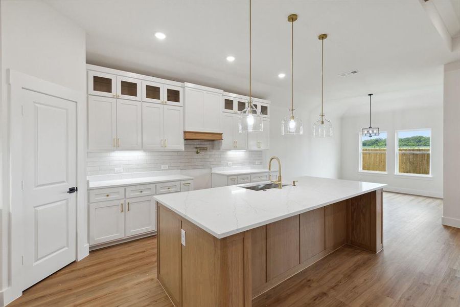 Kitchen featuring light wood finished floors, tasteful backsplash, white cabinetry, a sink, and a large island with sink