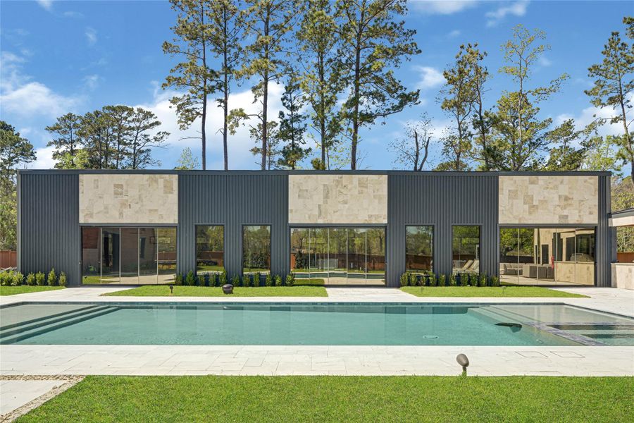 Minimalist design with large windows and a spacious layout. The backyard includes a pristine swimming pool, surrounded by lush greenery and tall trees, offering a serene and private outdoor space.